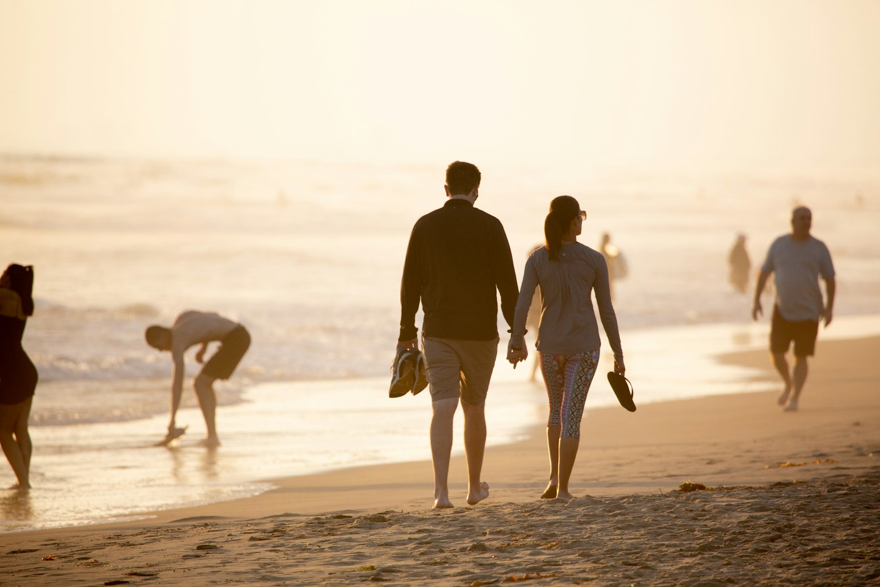 A couple walking a New Zealand beach at golden hour.