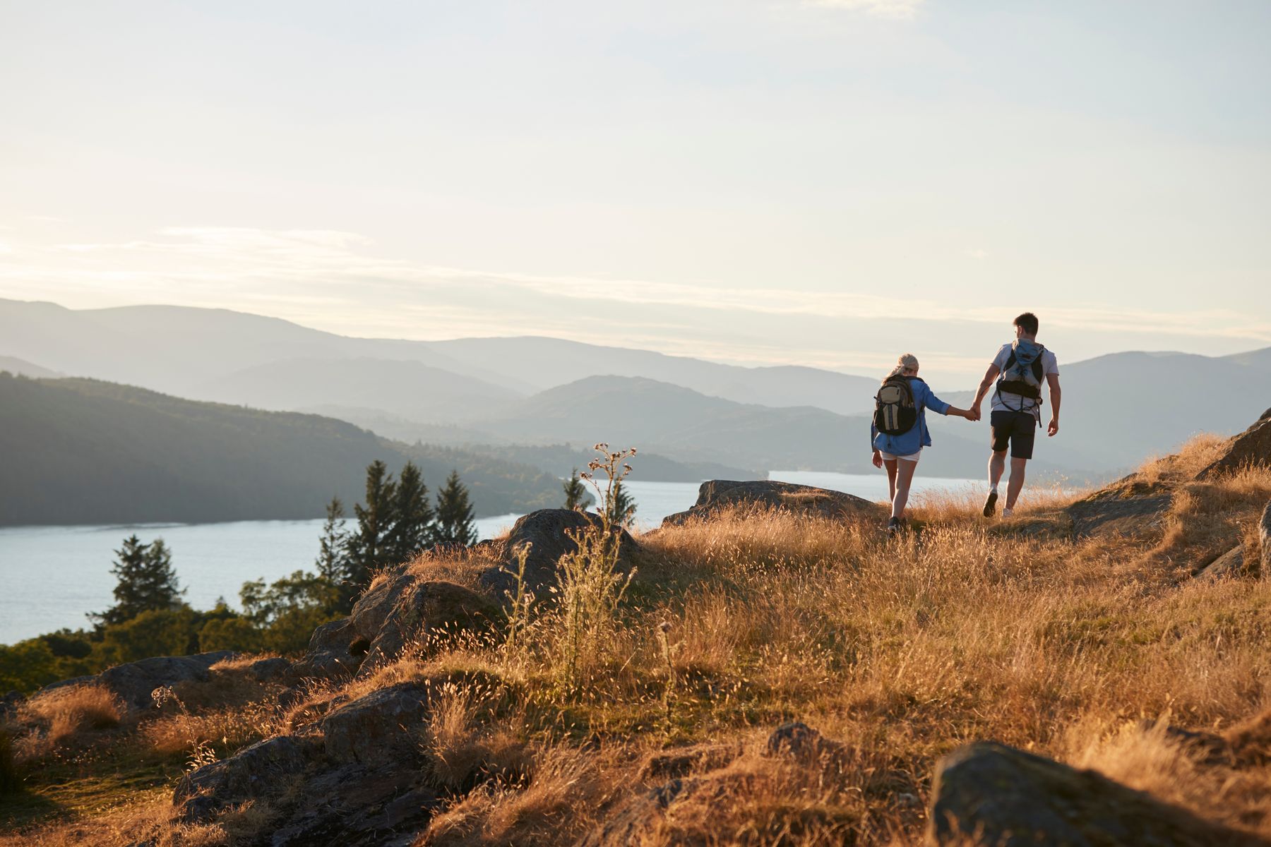 Two people walking a golden hilltop path towards a lake on the horizon.